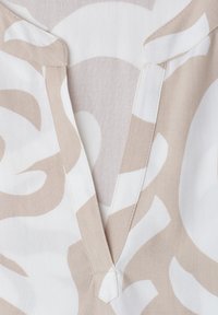 Primer plano de tela beige y blanca con patrón y cuello en V que muestra costuras detalladas y formas abstractas.