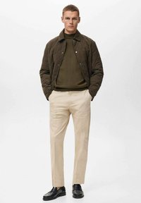 Kvaliteta olivno zelena jakna s prešito teksturo, temna jopica, bež hlače in črne čevlje. Ima zapenjanje s gumbi in prilegajočo se postavo. Gladek zaključek in strukturiran dizajn.