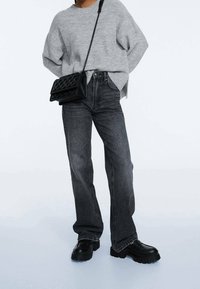 Gray oversized knit sweater, high-waisted dark denim jeans, black quilted shoulder bag, chunky black platform shoes.