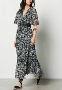 Svart och vit blommig maxiklänning med V-ringning, korta ärmar, smockad midja och flödande kjol; tillsammans med flätade svarta espadriller.