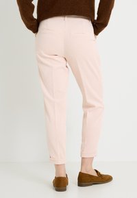 Pantalones de pana rosa claro con un corte entallado, bolsillos traseros y puños remangados, combinados con mocasines de ante marrón.