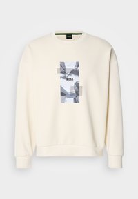 Sweat-shirt crème avec un graphique de paysage urbain en noir et blanc et le mot "BOSS" centré sur la poitrine.