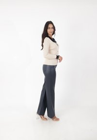 Cárdigan de canalé beige con detalles en negro, combinado con pantalones oscuros elegantes con aberturas laterales y sandalias transparentes de tacón bloque.