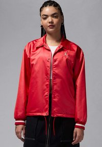 Punainen satiiniset bomber-takki, jossa napitettava suljin, pitkät hihat, valkoiset raidalliset hihansuut ja pieni logoyksityiskohta rinnassa.