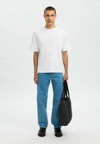 White short-sleeve t-shirt, blue straight-leg jeans, black shoes, and a black fabric tote bag with dual straps. Neutral background.