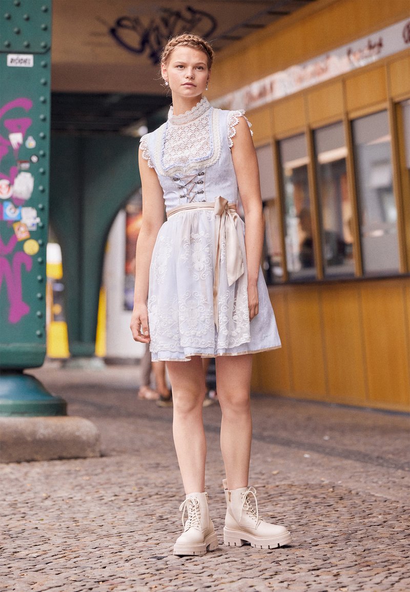 Helles blaues Kleid mit Spitze, floralen Stickereien und einem Bindegürtel, kombiniert mit beigen Schnürstiefeln mit einer klobigen Sohle.