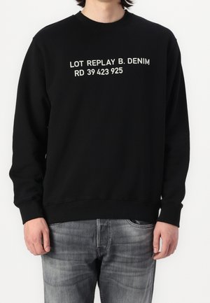 Černá mikina se širším výstřihem a žebrovanými manžetami. Na přední straně se nachází bílý text "LOT REPLAY B. DENIM RD 39 423 925".
