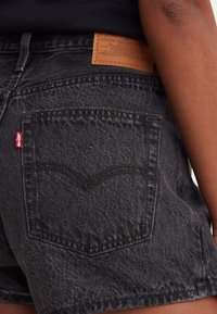 Svarta denimshorts med en bakficka som har Levi's röda etikett och en sandfärgad läderlapp ovanför midjan på en persons höft.