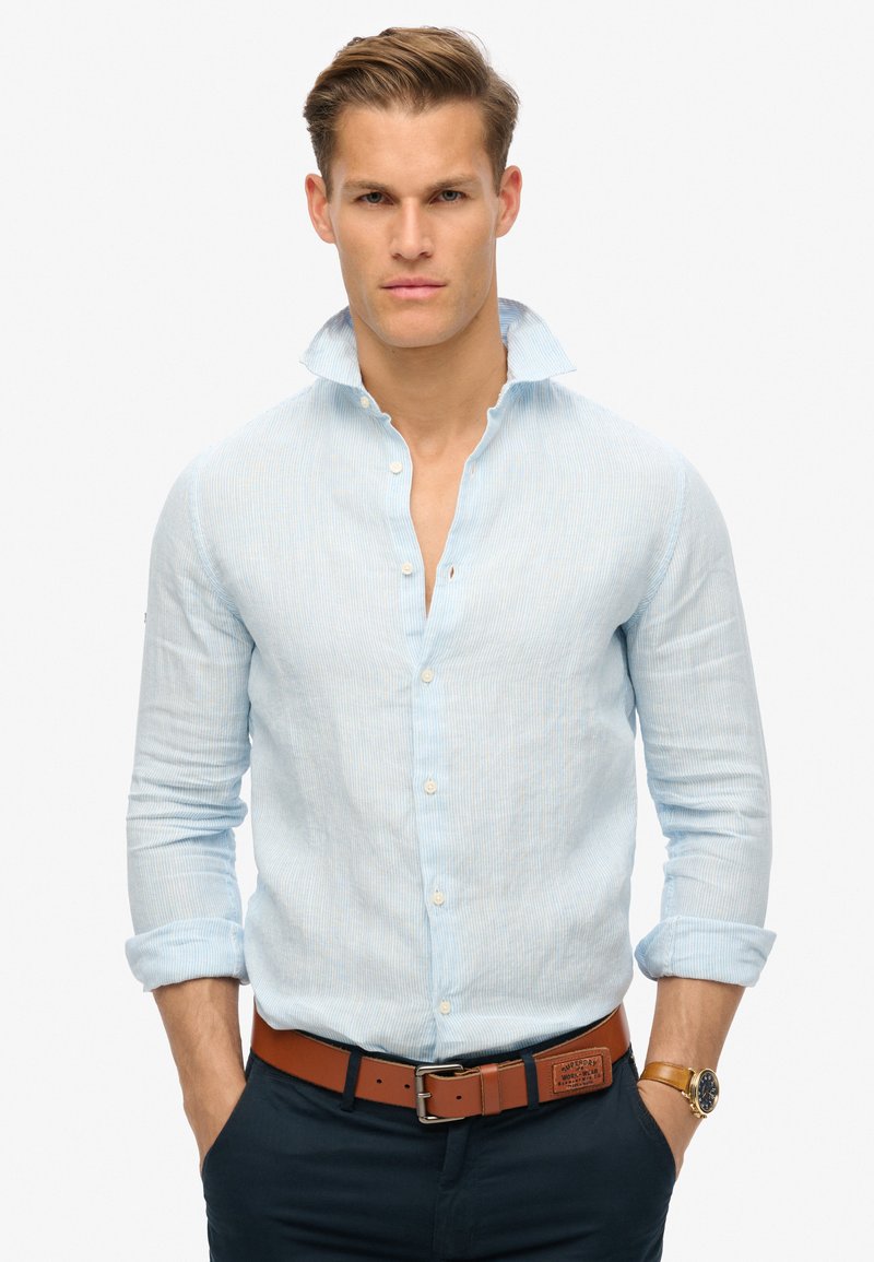 Lichtblauw gestreept overhemd met een spread collar, lange mouwen opgerold bij de manchetten, gecombineerd met een bruine leren riem en een marineblauwe broek.