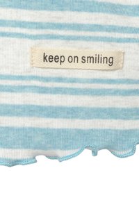 Gestreifter Stoff in Hellblau und Weiß; mit einer gewellten Kante und einem Etikett, das "Mach weiter zu lächeln" liest.