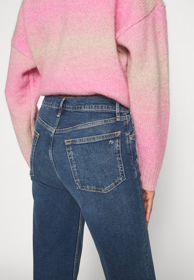 Jeans in denim blu scuro con vita alta, dotati di due tasche posteriori e dettagli di cucitura delicati, abbinati a un maglione in maglia con gradienti di colore rosa.