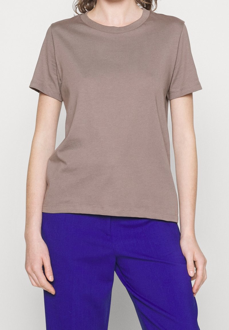 T-shirt en coton marron avec un col rond, des manches courtes et un logo Calvin Klein discret. Assorti à un pantalon bleu avec une texture lisse.