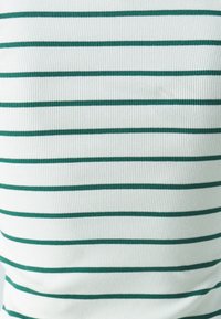 Top de tejido blanco acanalado con rayas verdes horizontales. La textura es ligeramente texturizada debido al detalle acanalado.