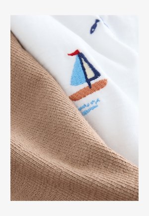 Pamut anyag, amely egy világosbarna texturált részt mutat, amely átfedi a fehér anyagot, melyen kék és piros hímzett vitorlás hajó díszítés látható.