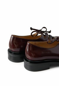 Scarpe in pelle bordeaux con finitura lucida, punta rotonda e suola nera spessa. Presentano lacci a fiocco e un design intagliato nella parte anteriore.