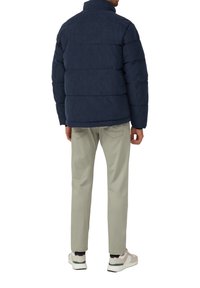 Marineblaues Puffermantel mit hohem Kragen, gestepptem Design und langen Ärmeln, kombiniert mit hellbeigen Hosen und weißen Sneakern.