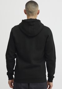Sudadera con capucha negra hecha de tela suave, con mangas largas y un corte relajado. El diseño incluye un dobladillo y puños acanalados.