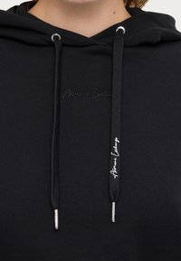 Felpa con cappuccio nera realizzata in un tessuto testurizzato, con lacci dotati di estremità metalliche e logo ricamato sul petto.