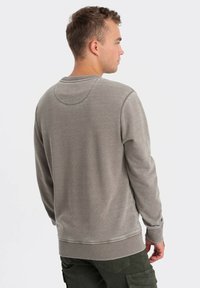 Šedá mikina s jemnou texturou, kulatým výstřihem a žebrovaným lemem. Má dlouhé rukávy a čistý, minimalistický design.
