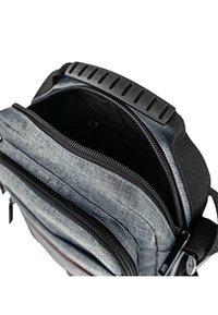 Bolsa mensajera de tela gris con múltiples compartimentos con cremallera, herrajes negros, una superficie texturizada y un asa acolchada en la parte superior.