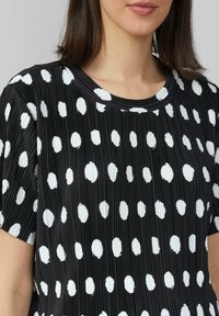 Zwart geplooid top met witte onregelmatige stippen, ronde halslijn en korte mouwen, met een gladde textuur en casual ontwerp.