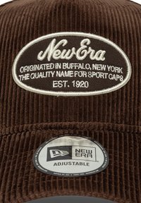 Braune Cordmütze mit einem gestickten ovalen Patch, auf dem "New Era" steht. Verstellbar mit einem runden Logosticker auf dem Schirm. Texturiertes Material.