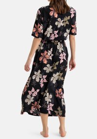 Robe maxi florale à manches courtes, fond noir, dotée de fleurs roses, blanches et beiges, en tissu texturé, avec une taille cintrée par un lien.