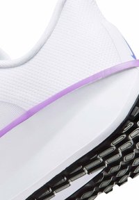 Chaussure de sport blanche avec une tige texturée, présentant un accent violet sur le côté et une semelle noire à motif pour la traction.
