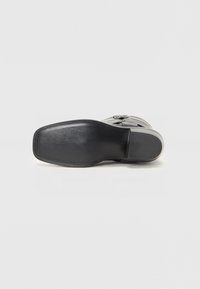 Suela de zapato negra con una superficie lisa y plana y una ligera curvatura en el talón; presenta una mínima marca y un borde texturizado.