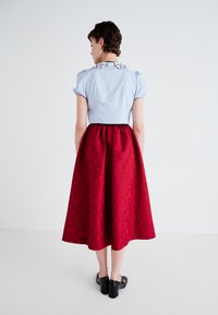 Light blue fitted top with puff sleeves and black floral embroidery. Red textured skirt with a floral pattern, paired with black shoes.