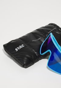 Des lunettes de soleil bleues avec une forme angulaire unique, reposant sur un étui rembourré noir portant des accents de texte et de logo blancs.