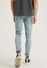 Jean de mezclilla azul claro con un corte ajustado, textura deslavada y bolsillos traseros. Combinado con zapatos oscuros y una camiseta gris oscura.