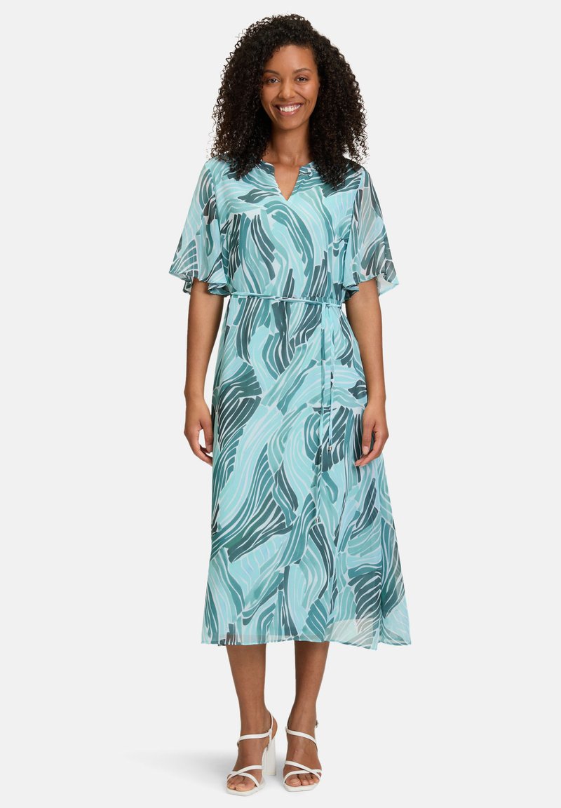 Ein halbtransparentes, türkisfarbenes Kleid mit abstrakten dunkelgrünen Wellenmustern, kurzen, schwingenden Ärmeln und einer taillierten Taille, das bis zur Mitte der Waden reicht.