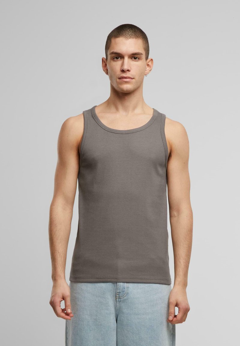 Grå ribbet tanktopp med rund hals, vist på en person som har på seg lyse denimshorts. Materialet ser glatt og elastisk ut.