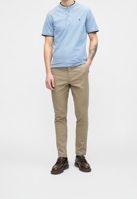 Světlomodré polo s krátkým rukávem a černým lemováním, kombinované s béžovými úzkými kalhotami a hnědými šněrovacími botami. Minimalistický design, ležérní styl.