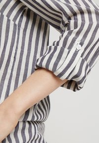 Camicia a righe con bottoni, caratterizzata da strisce orizzontali blu navy e bianche, tessuto leggero e maniche arrotolate con chiusura a bottoni.