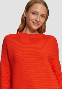 Leuchtend orangefarbener, gestrickter Pullover mit geribbelter Textur, runder Halslinie und tiefen Schultern. Leicht und lässig im Design.