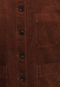 Brun fløjlsvest med lodrette ribber, fem sorte knapper og to frontlommer på venstre og højre side.