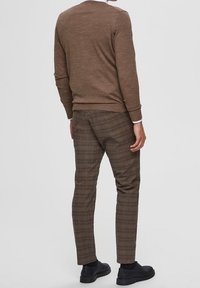 Brauner Pullover mit geripptem Saum, kombiniert mit braunen karottenförmigen Hosen mit dünnen blauen Linien, abgerundet mit schwarzen Schuhen.
