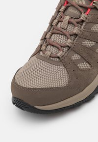Brązowy but trekkingowy z cholewką z siateczki i zamszu, kontrastującymi czerwonymi sznurówkami, wyściełanym kołnierzem oraz czarną, teksturowaną gumową podeszwą.