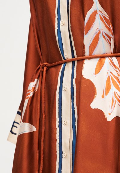 Φόρεμα σε σκουριά απόχρωση με λευκά, μπλε και πορτοκαλί αφηρημένα φύλλα, κουμπιά στο μπροστινό μέρος και λεπτή ζώνη που δένει στη μέση.
