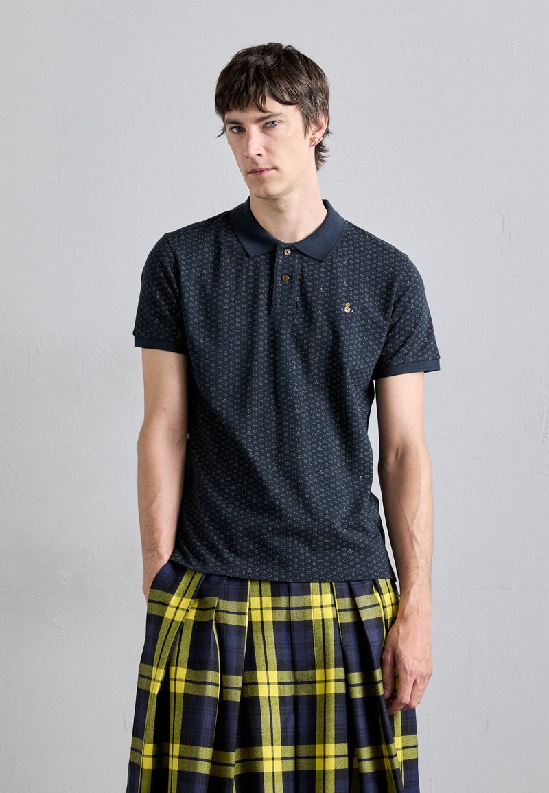 Marineblaues Poloshirt mit strukturiertem Muster, Drei-Knopf-Leiste und Logodetail. Kombiniert mit einem gelb-marineblau karierten Faltenrock.