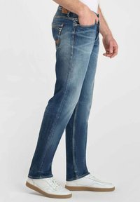Jeans de mezclilla azul claro con un corte recto, que presentan un lavado desgastado, costuras visibles y diseño de cinco bolsillos, combinados con zapatillas blancas.