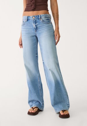 Hellblaue, weit geschnittene Jeans aus Denim, mit einem ausgewaschenen Look, fünf Taschen und Ziernähten. Tragen Sie flache Sandalen dazu.