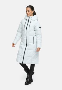 Long light blue puffer coat with a hood, black zip closure, side pockets, and black accents. Paired with black pants and boots.