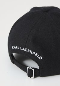 Casquette en feutre noir avec un bord courbé, ornée d'un texte brodé blanc "KARL LAGERFELD" à l'arrière et d'une fermeture à boucle ajustable en argent.