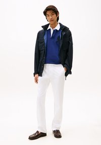 Ναυτικό αδιάβροχο μπουφάν, μπλε πόλο με κεντημένη λεπτομέρεια, λευκό παντελόνι και σκούρα λοφάρια. Ομαλές υφές και δομημένος σχεδιασμός.