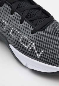 Černá a šedá sportovní obuv s prodyšným svrškem z síťoviny, texturovanými tkaničkami a bílou mezipodešví s detailem na boku.