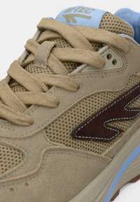 Bež atletski tenisica s mrežastim gornjim dijelom, detaljima od antilopa, smeđim logotipom, ravnim vezicama i svijetloplavim obrubom uz đon.