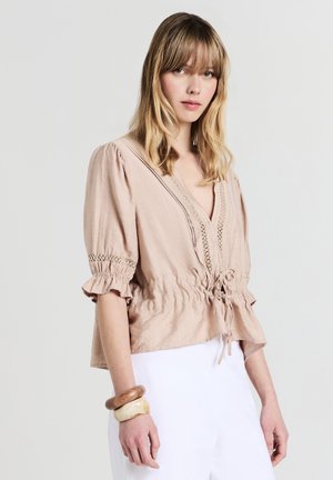 Blush pink blouse with a V-neck, puff sleeves, and gathered waist. Features lace details and a drawstring at the hem. Lightweight fabric.